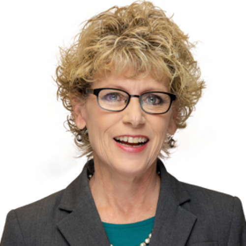 Description of Shannon Paige: Shannon is an older woman with short blonde hair. She wears black glasses, a dark grey blazer and a teal blouse in front of a white background. 