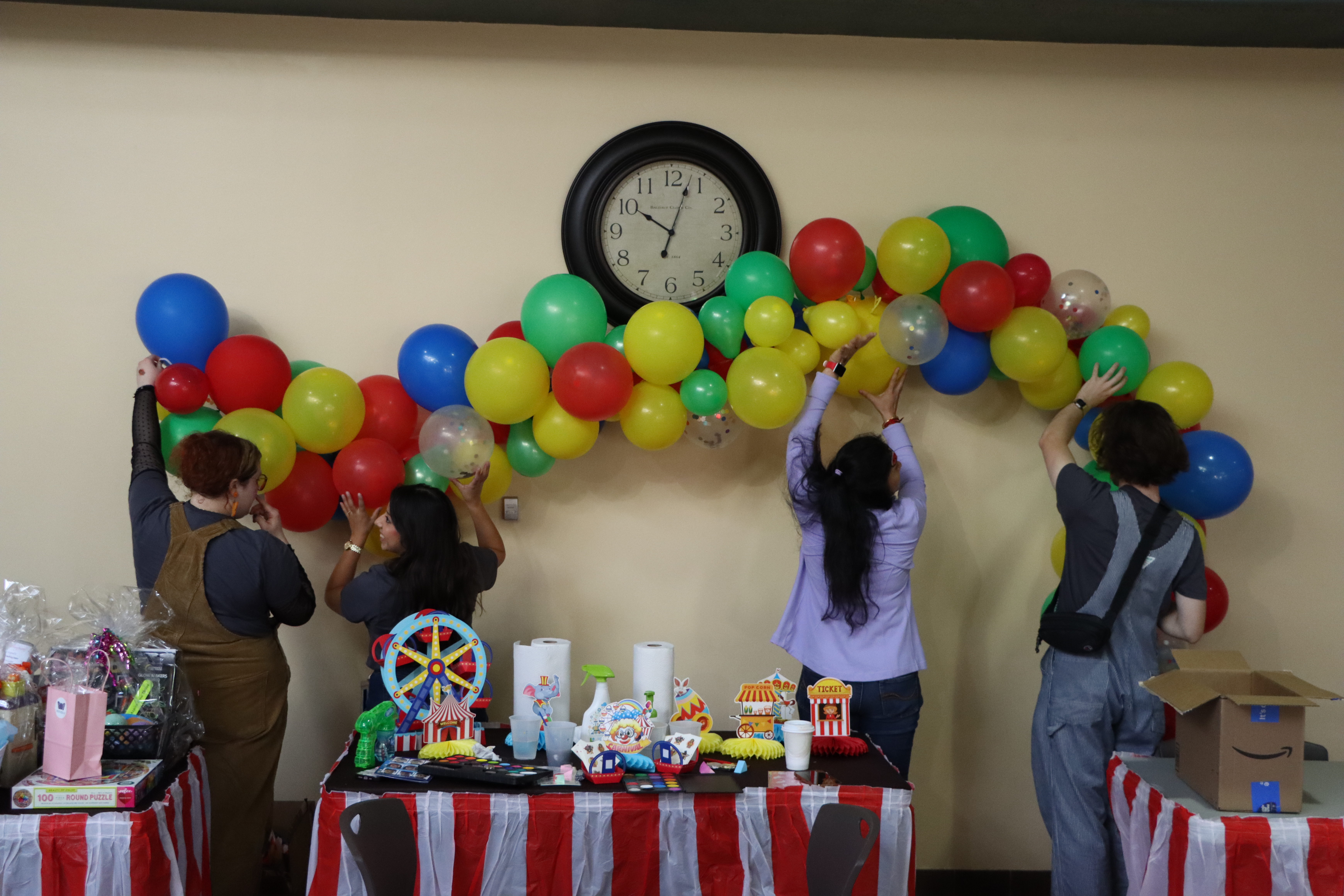 four people putting up a rainbow balloon banner