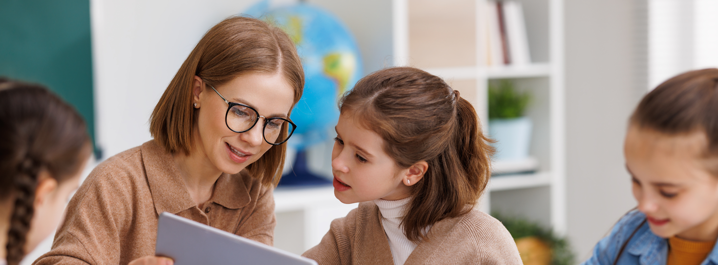 Researcher with tablet engages with children at a table. 