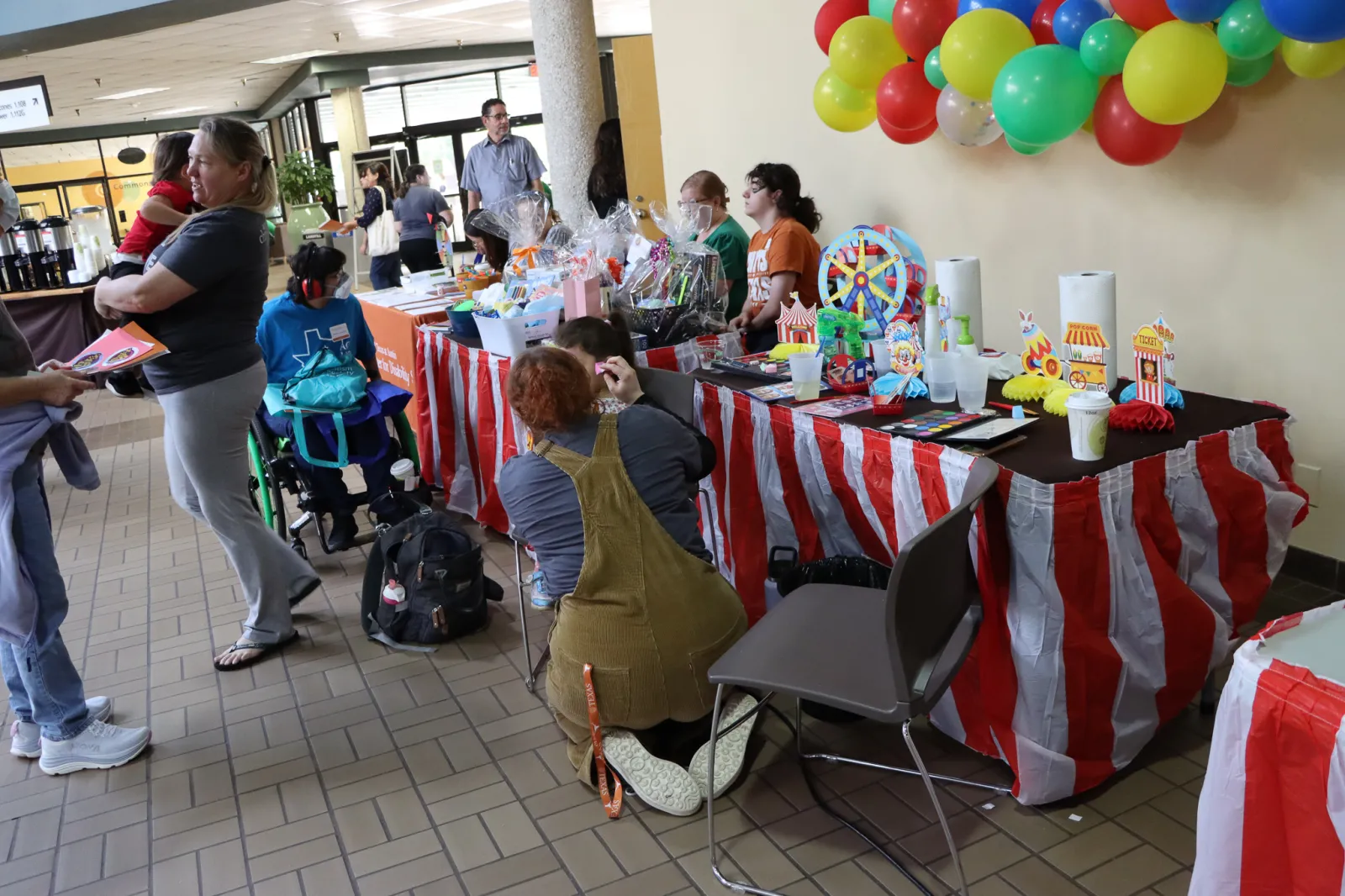 A face painting station with a carnival theme, including a red and white striped tablecloth and balloons.