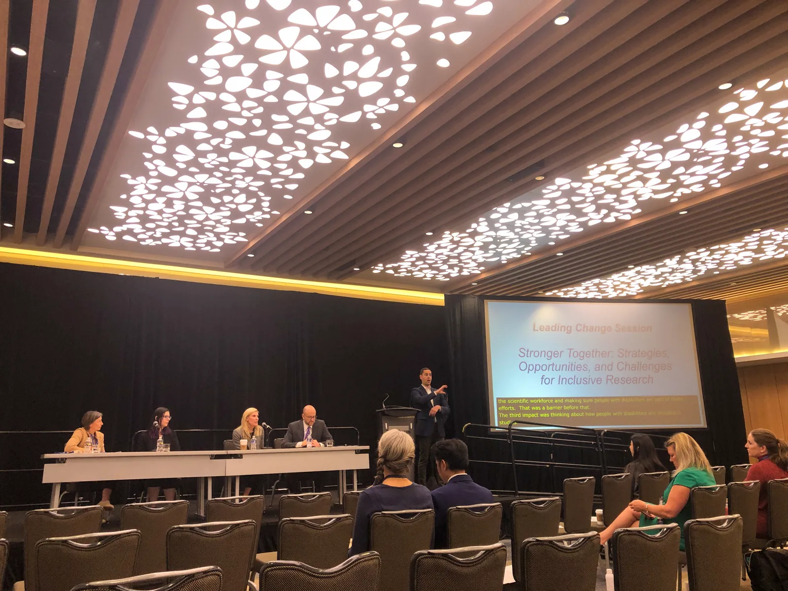 Leading Change session. Onstage are three female panelists and one male. Stage left is a sign language interpreter by the presentation screen.