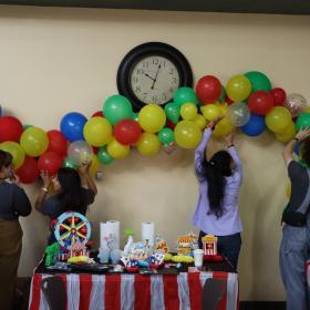 four people putting up a rainbow balloon banner