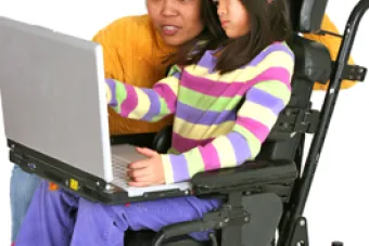 Lady assisting girl in wheelchair with laptop computer