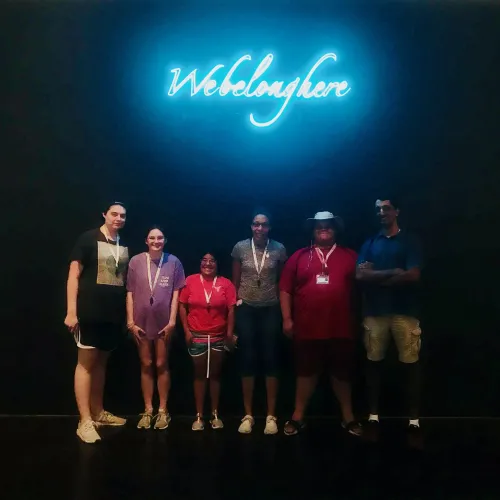 6 E4 students standing below a blue neon sign with the words "we belong here" beneath it