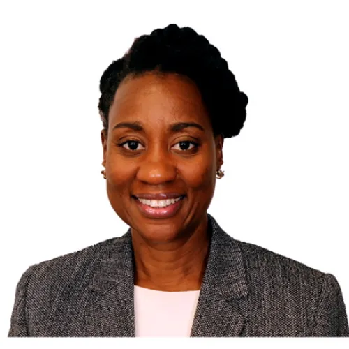 Description: Angela McCarty is black woman with a braided up-do; she wears a grey blazer and a white blouse.