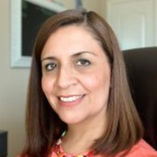 Rosalba has shoulder length brown hair and wears a salmon colored blouse.