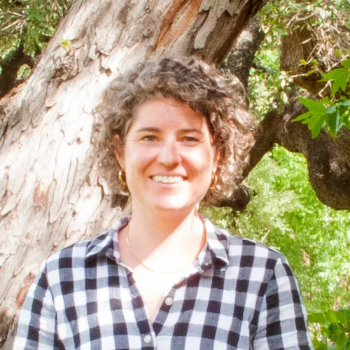 Sarah has short, curly brown hair. She wears a gingham shirt with white and black squares. 