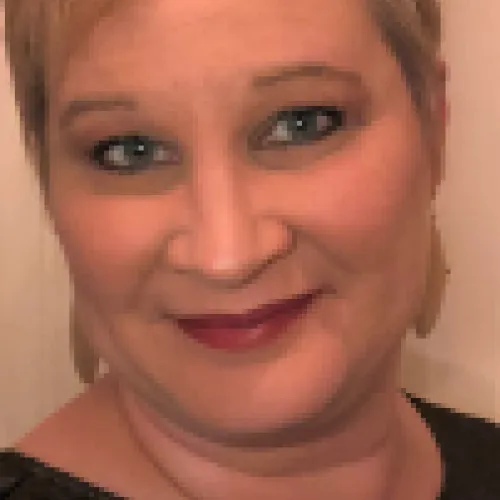 Description: Cynda has short cropped blonde hair and wears a black blouse. 