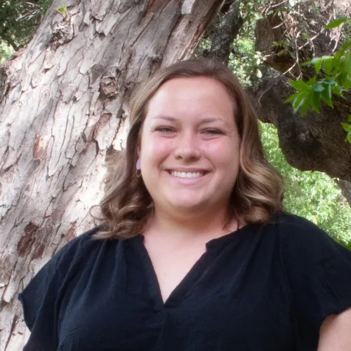Alex Nolan has shoulder-length brown hair and wears a black blouse. 