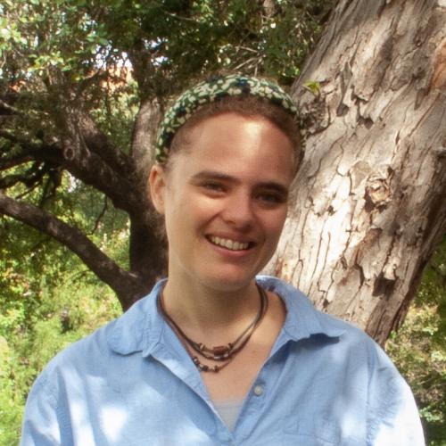 Catherine Harwood has brown hair tied in a bun; she wears a light blue shirt and a bandana. 