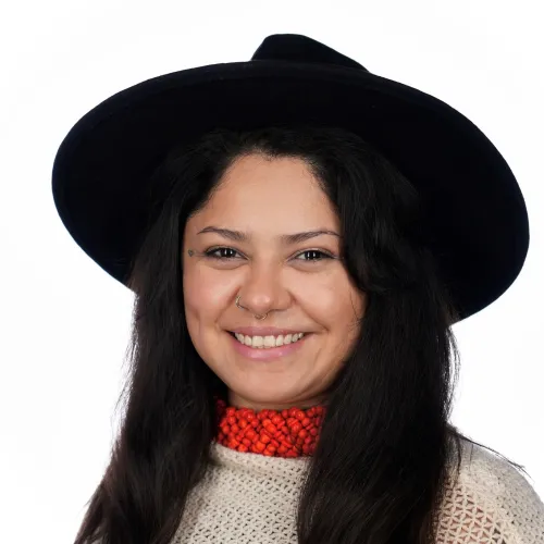 Image of Kiki Avilez. She has long, black hair and wears a black, wide-rimmed hat, a beige blouse and a red necklace. 