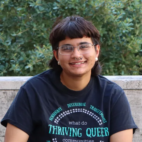 Naksh in a non-binary individual with a fashionable mullet, glasses and nose and ear piercings.