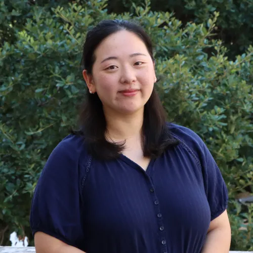 Younghwa has shoulder length black hair. She wears a dark blue dress. 