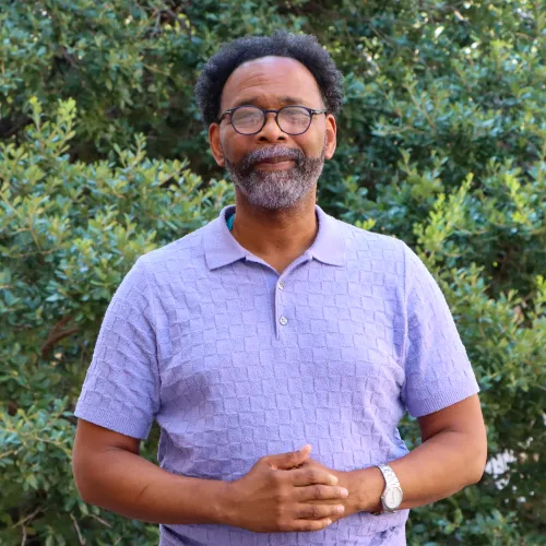 Don is an older black gentleman with dark hair and a salt and pepper beard. He wears a purple polo shirt and round framed glasses.