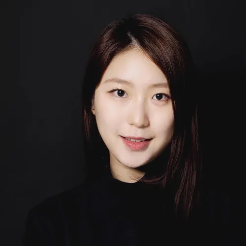 Jane is a young Asian woman with dark brown hair. She wears a black sweater in front of a black background.
