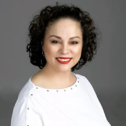 A person with curly hair smiling and wearing a white shirt.