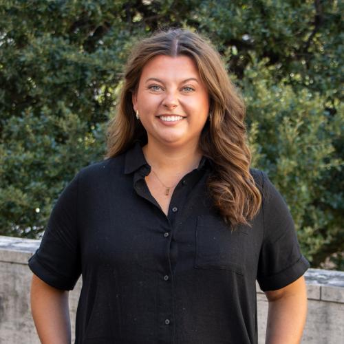 Kyleigh has wavy brown hair. She wears a black, button-down dress. 