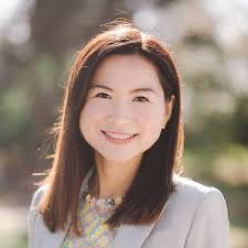 Amy has a business coat on with dark, reddish hair and softer features