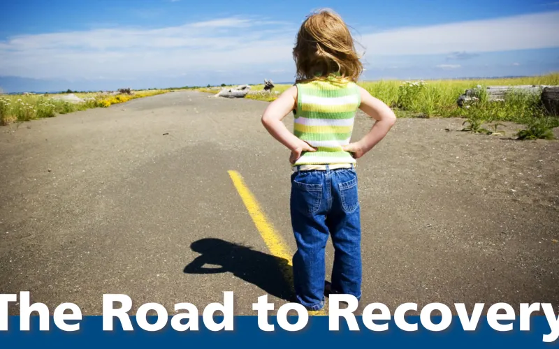 a child with hands on hips looking down an empty county road